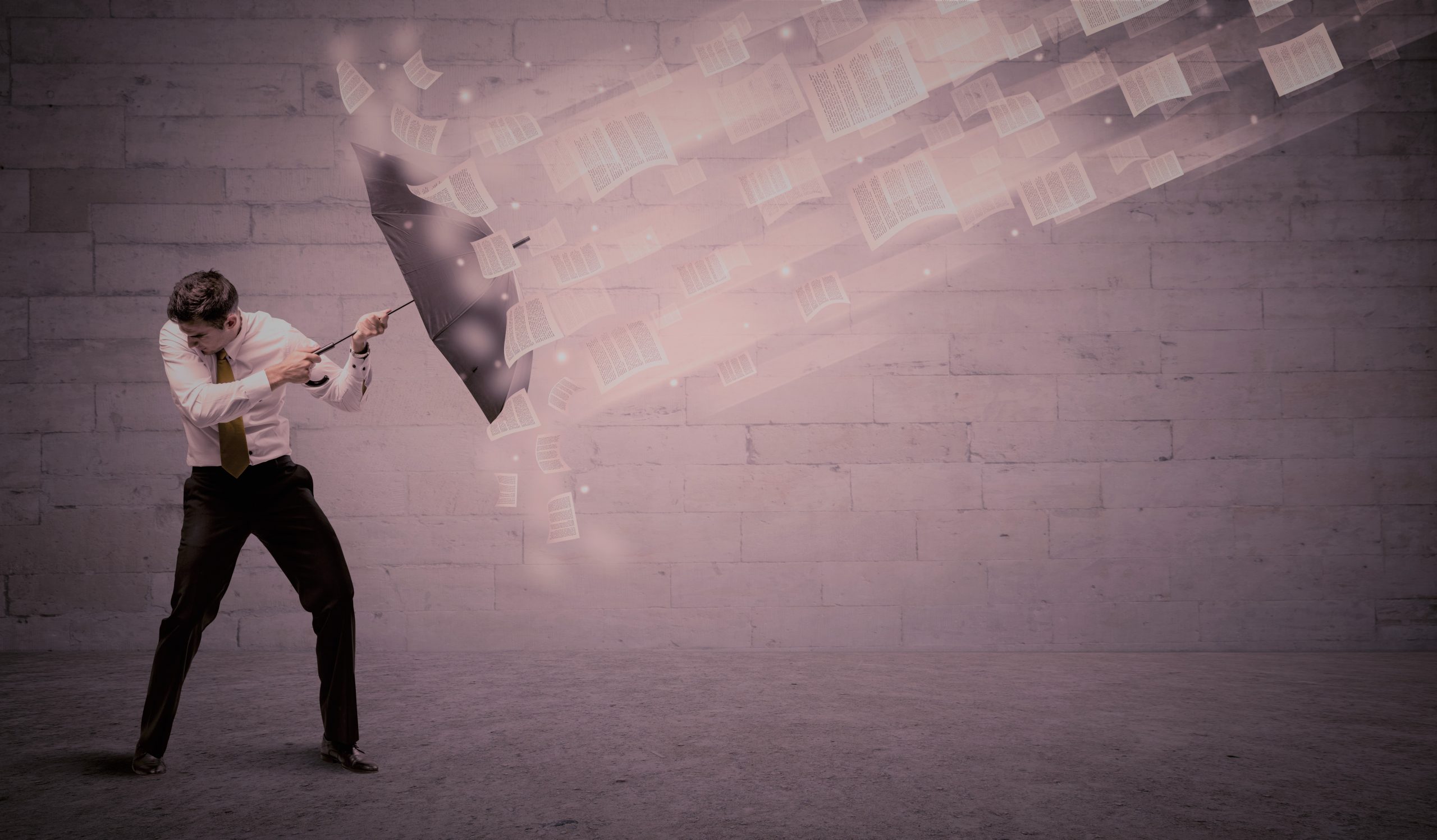 Business man protecting with umbrella against wind of papers
